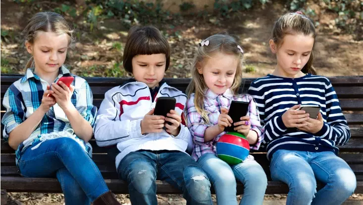 four kids sitting on a bench and using mobile phones