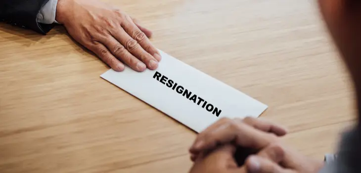 Two hands on a table and a resignation letter between them